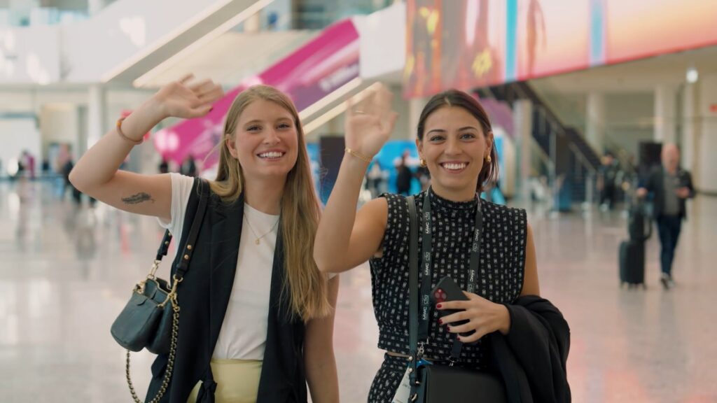 two young girls are smiling and waving at the camera as they walk down