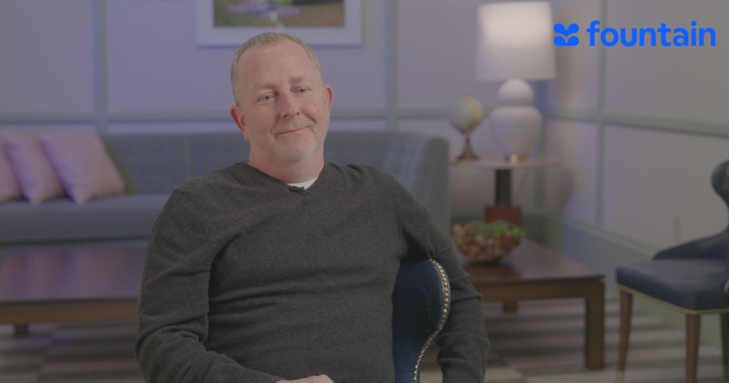 a man wearing a sweater is seated for an interview