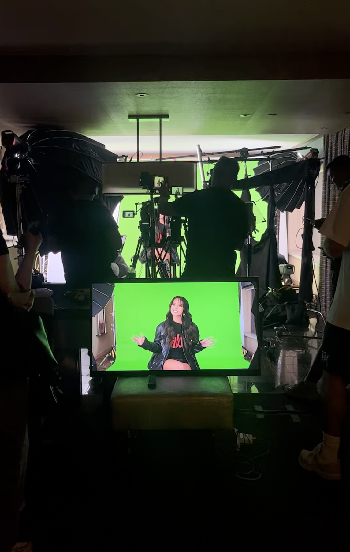 a woman on a green screen is stated talking into the camera while professional crew is behind cameras