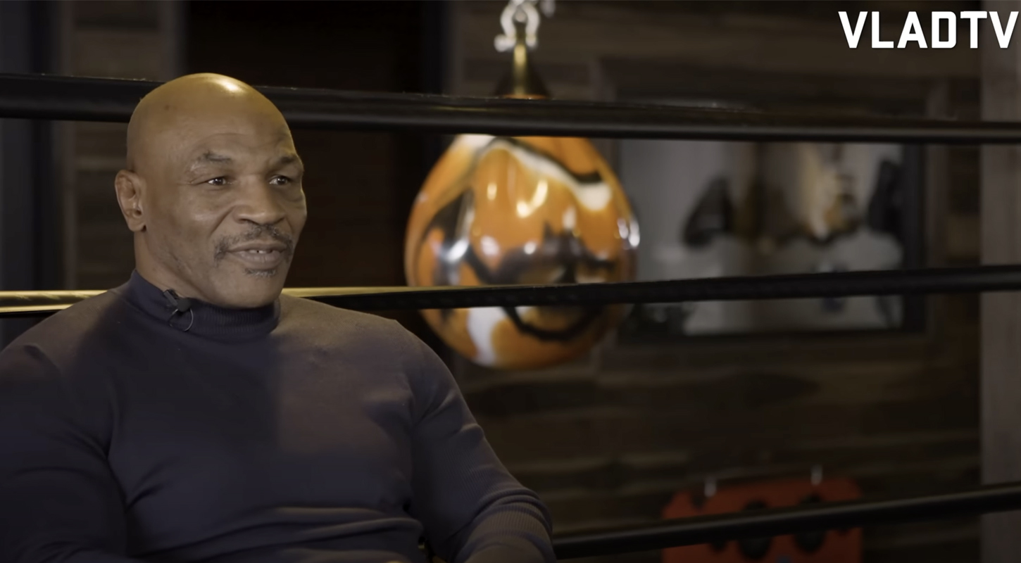 mike tyson sits inside a ring giving an interview with a boxing bag behind him