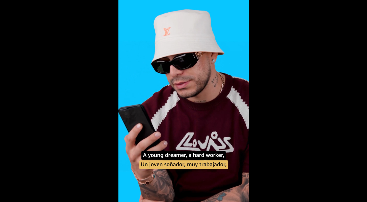 a person in a hat against a blue screen is holding a phone reading something . he is wearing sunglasses and a burgundy sweater