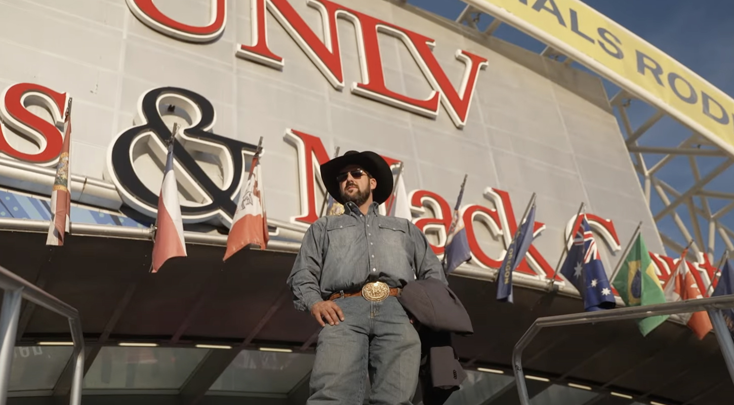 a cowboy in a cowboy heat and jeans is standing in front of UNLV Thomas and Mac center during sunrise