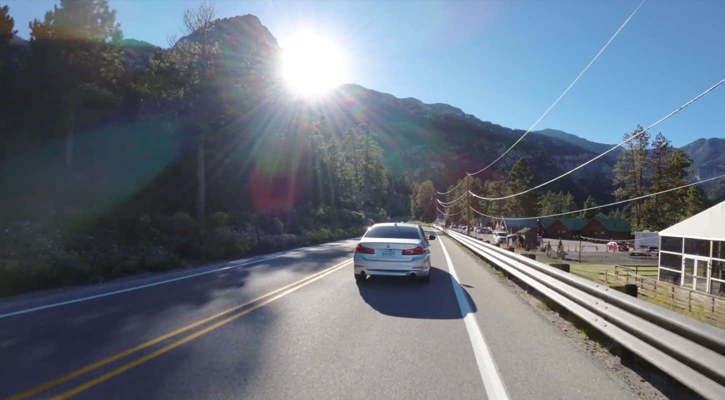 a silver bow is driving down a rural road with the sun in in front of it