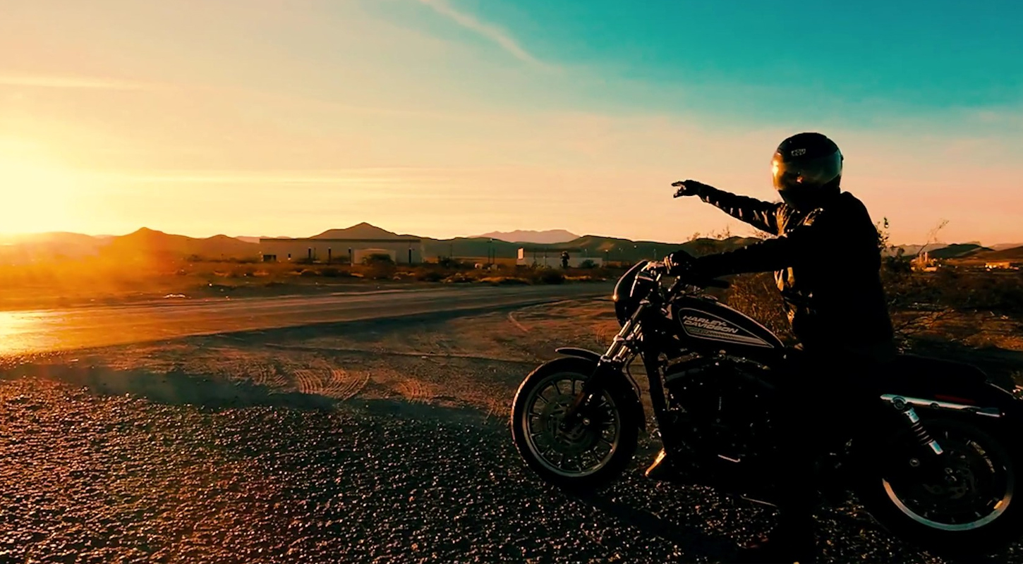 a person on a motorcycle is pointing into the distance toward the sunset on a rural road