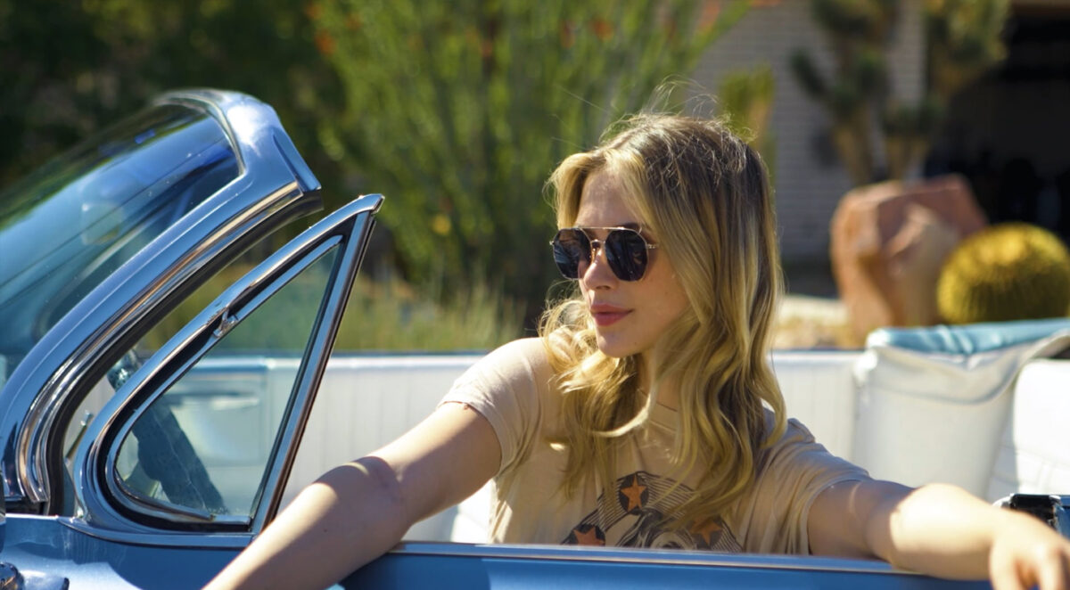 a young white woman in sunglasses is thinking about her future as she sits in a blue convertible car