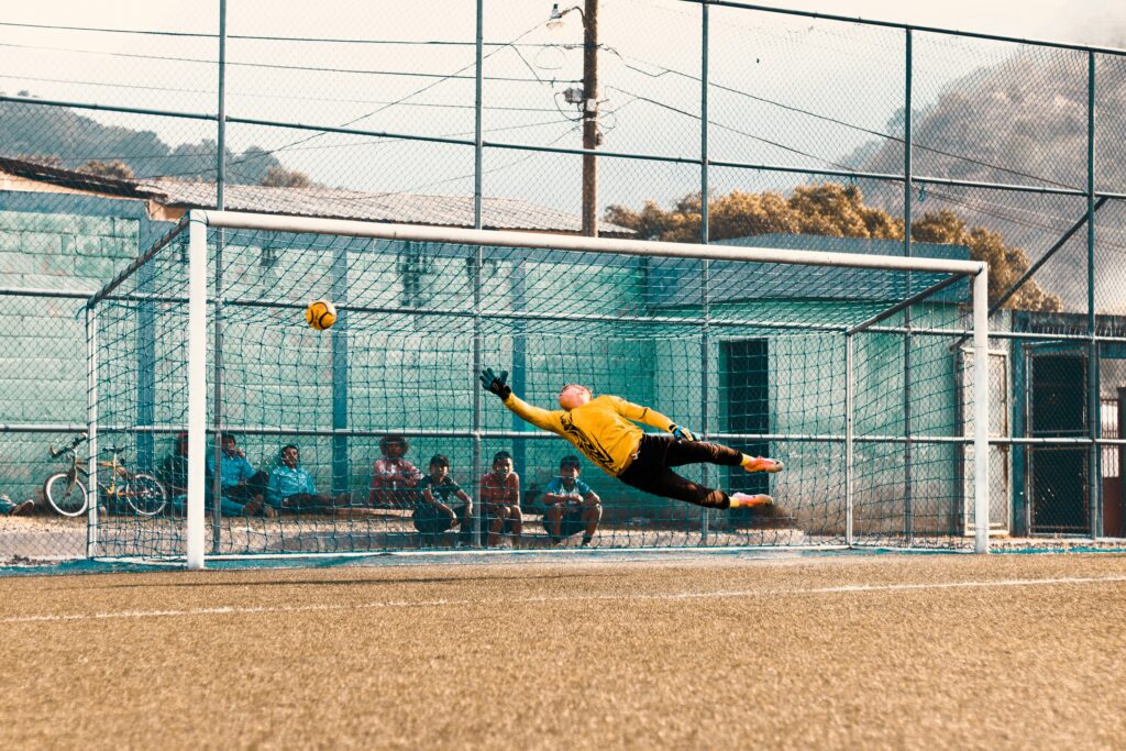 Goal defender diving to catch the soccer ball from making the goal