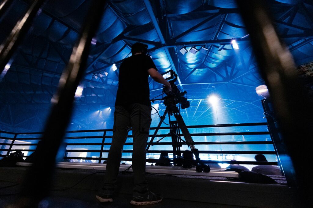 A camera crew operator standing at the rear of the venue