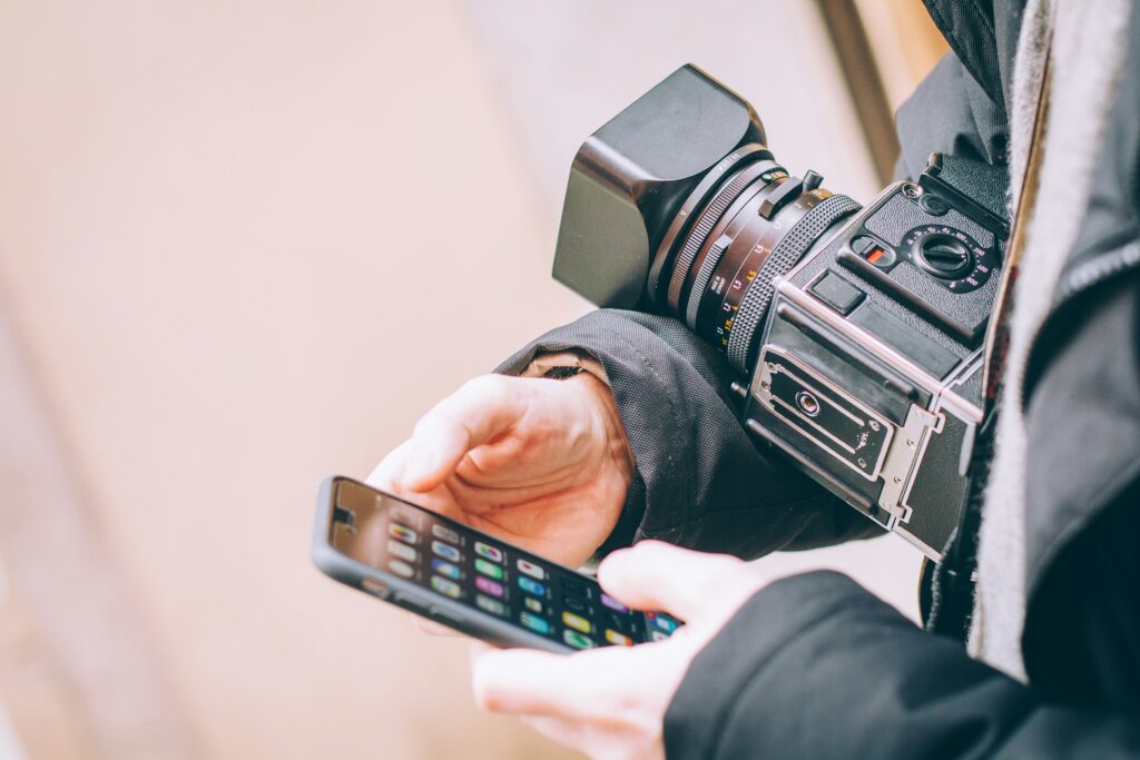 A camera operator holding both a camera and a phone